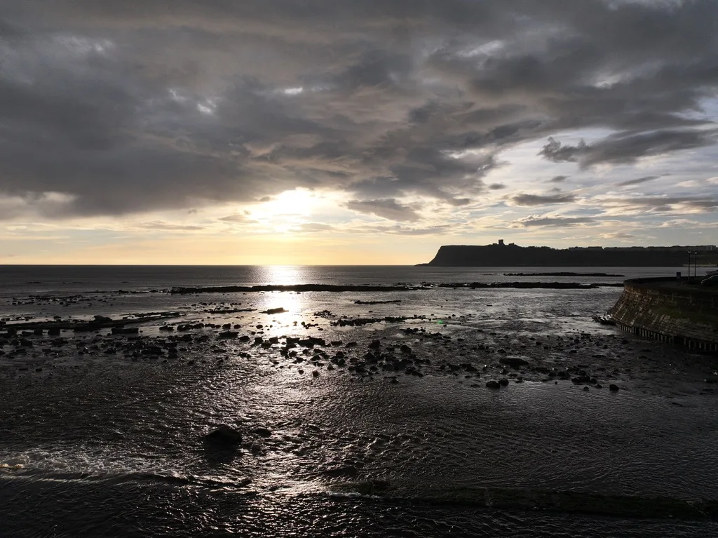 North Bay Scarborough just after sunrise with dramatic sky, low tide shoreline and castle headland in the distance