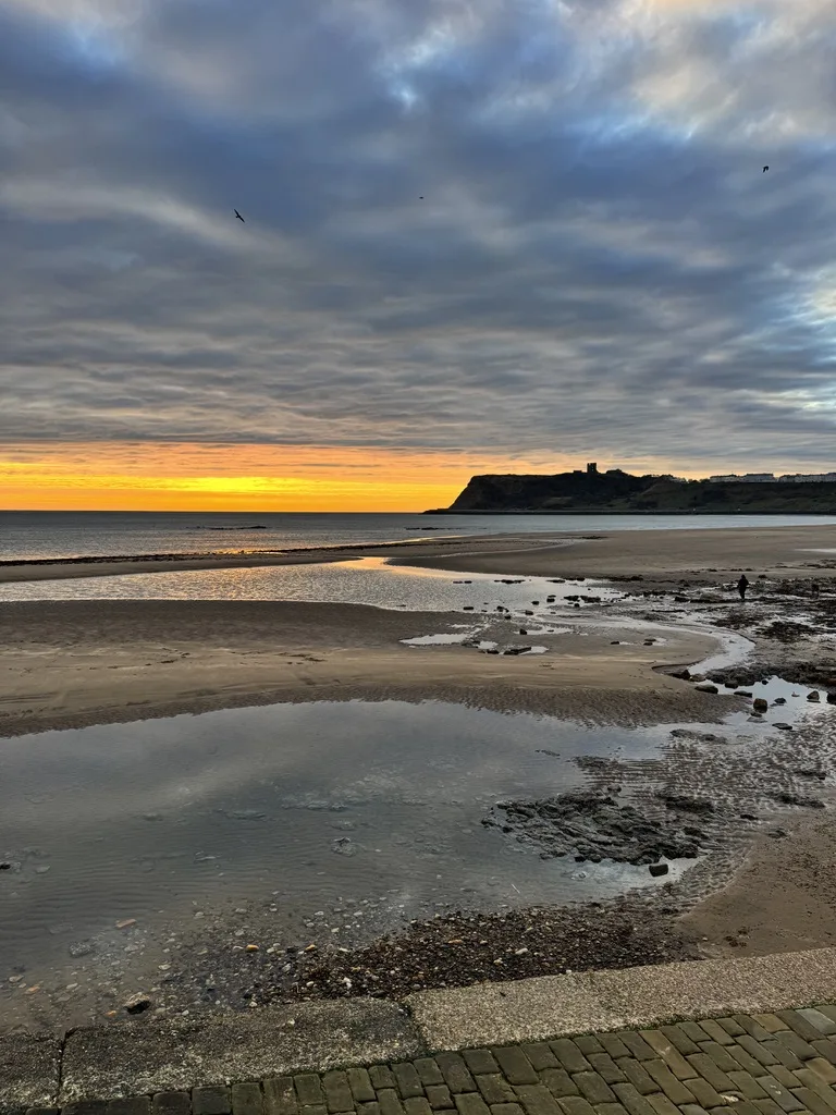 Sunrise over Scarborough North Bay beach with reflections in the sand and castle headland in the distance