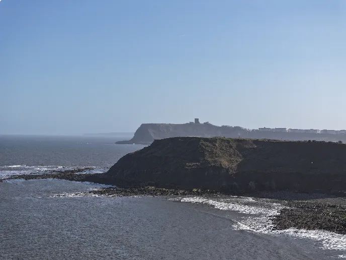 Golden autumn light over the Yorkshire Coast near Scarborough, with dramatic cliffs, rocky shoreline and calm sea under a clear blue sky